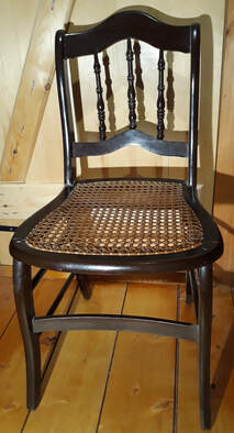Picture: 29 – A Jericho chair. Two of the characteristics of a Jericho chair are the flat curved stretcher between the front legs, instead of a round spindle, and the fact that the seat frame has the front chair legs sitting on the caning. The seat frames were made at the factory, and then sent out to area homes, where women and children could weave the cane seats as a cottage industry to make extra money for their family. They then were returned to the factory, where the assembly was completed, putting the legs on the caning. This makes a chair difficult to re-cane today, as these corner holes are covered by the legs.